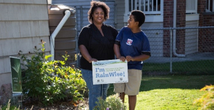 Woman and boy smiling and standing on a lawn in front of a Rainwise sign