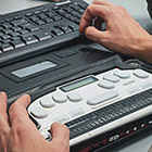 A man uses a Braille keyboard with a computer