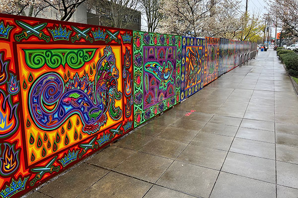 Colorful mural mounted along the length of a chainlink fence.