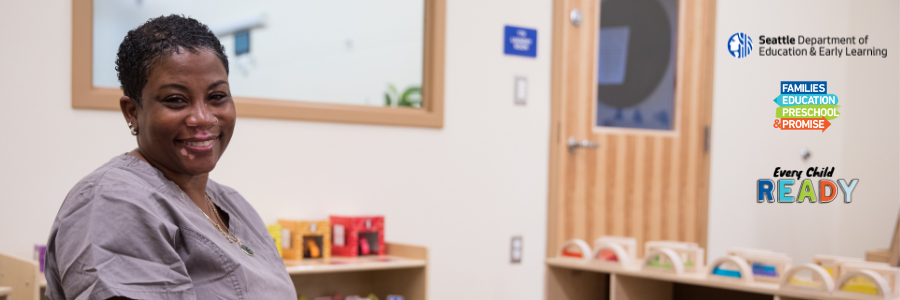 Smiling Black woman childcare worker with short black natural hair, vitiligo, and gray uniform.