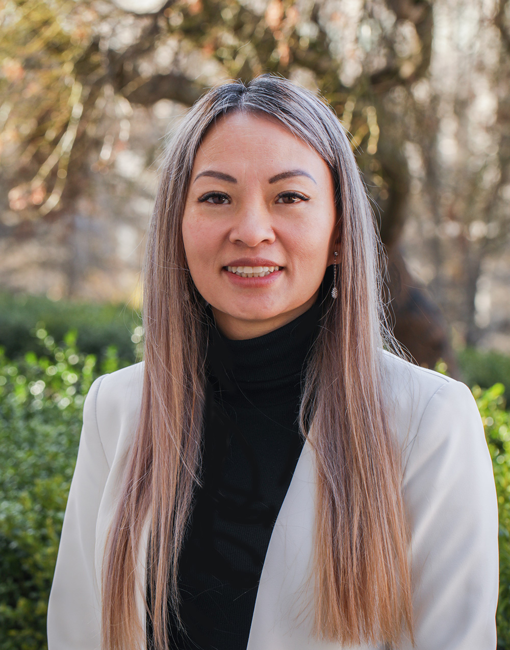 image of Jenifer Chao, a Southeast Asian woman with long brown/blonde hair. She is smiling and wearing a black turtleneck top under a grey blazer.