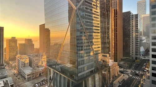 A tall, shiny building in downtown Seattle at sunset, surrounded by streets with cars and other buildings