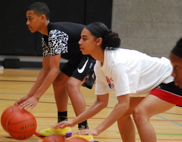 a boy and a girl crouch on an indoor basketball court, preparing to do drills