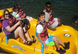 An adult with three preteens in a paddleboat on a lake, all wearing life jackets.