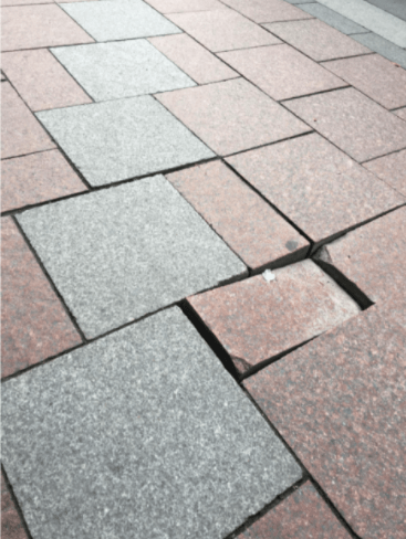 由灰色和粉紅色鋪路磚建造的人行道，其中一塊鋪路磚在腳踩時滑動。
