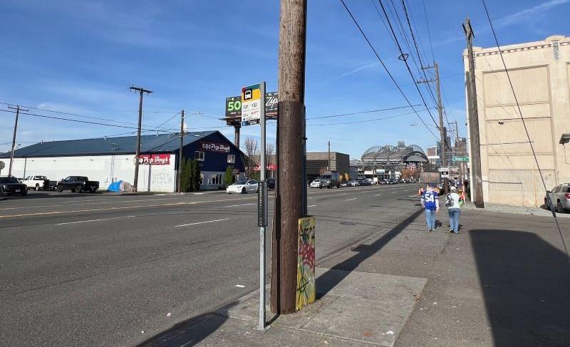 Two people walk north along 4th Avenue South on a sunny day, crossing South Walker Street near the Route 131 and 132 bus stop. 