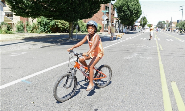 A school age girl on an orange bike smiles at the camera on a sunny day