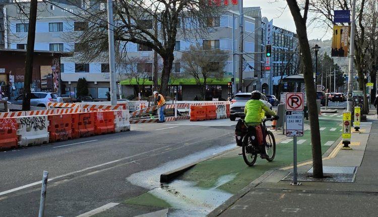 Image shows a cyclist passing crews in the University District as they place new sidewalks.