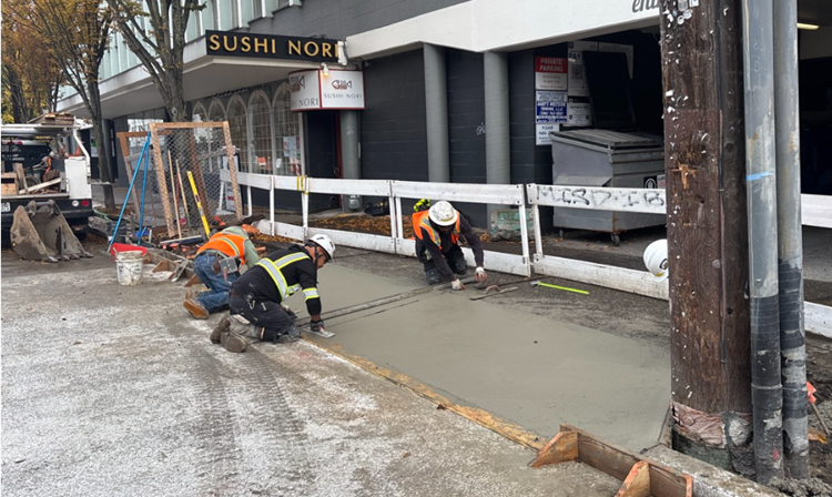 The image shows construction workers creating a new concrete driveway apron along Eastlake AVe E