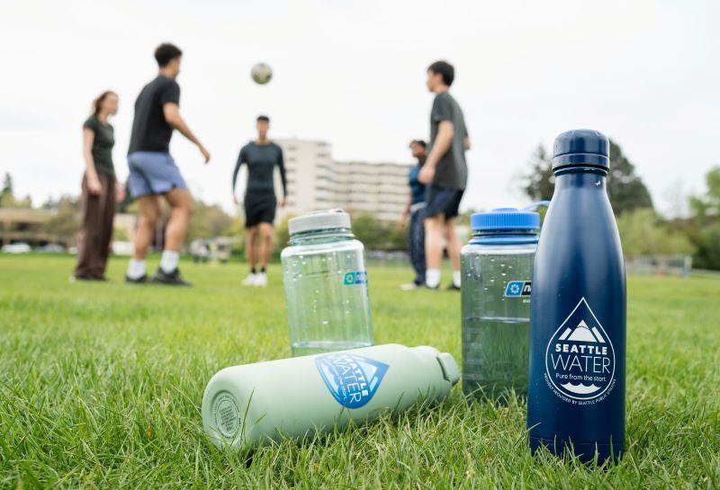 People kicking a soccer ball with reusable water bottles nearby.