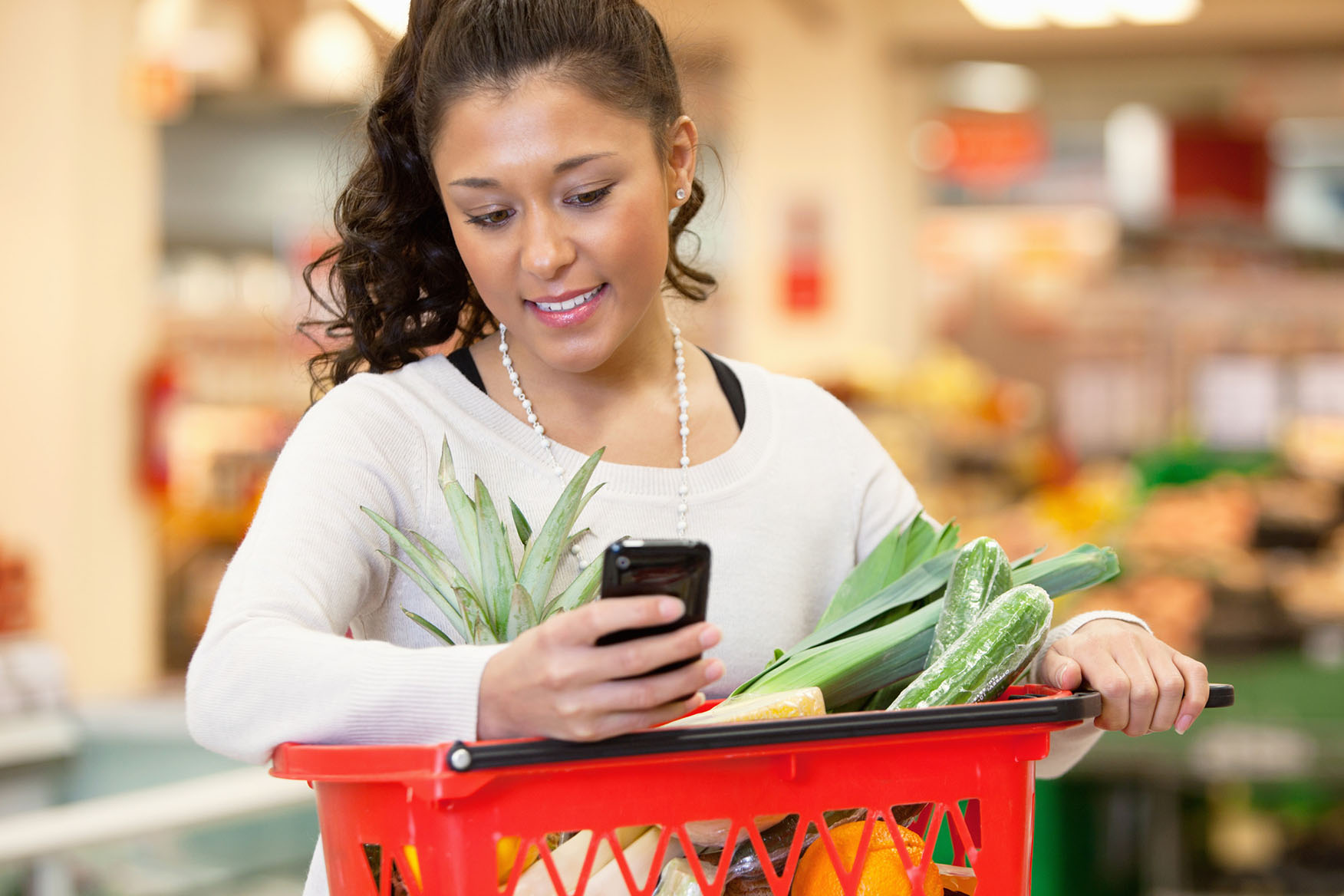 Woman checking shopping list on her phone while she holds a grocery basket