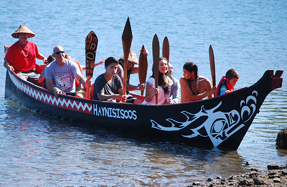 The traditional Native canoe 'Haynisisoos' pulls up at shore with paddles up.