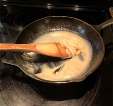 Iron pan on stovetop with wooden spoon and cooking fat.