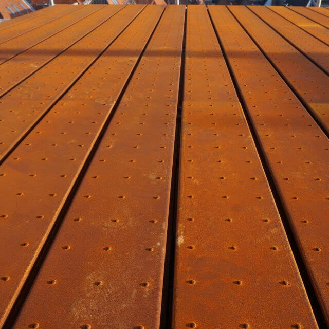 Closeup of steel planking with raised traction dots, in an orange rust color.