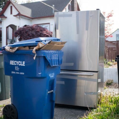 A refrigerator near a recycling bin.
