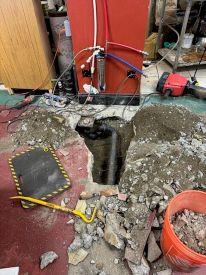 A section of torn up floor with an exposed pipe under the concrete