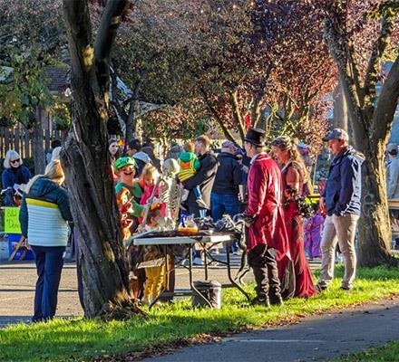 Tables with candy are set along a closed street full of people in costumes