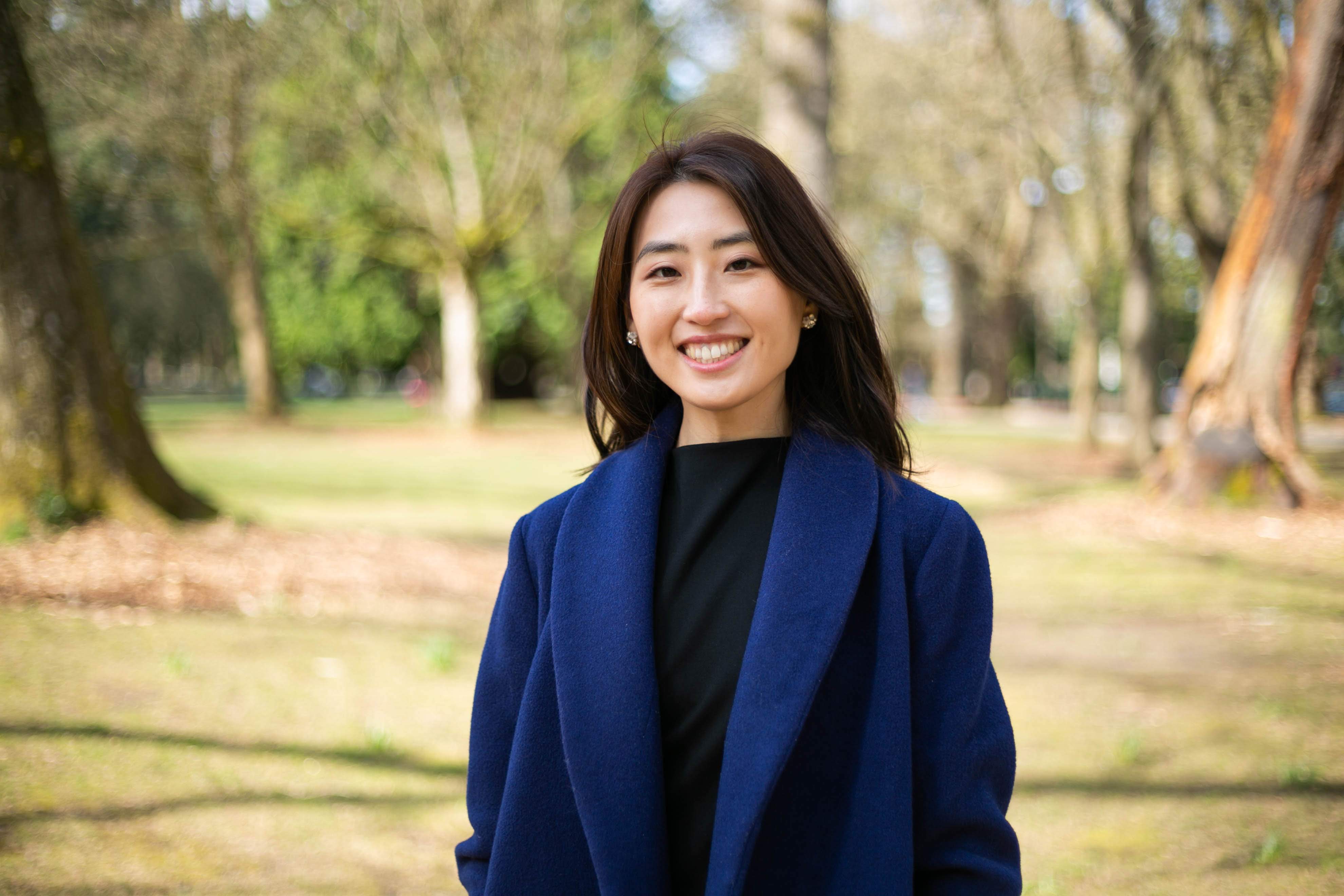 Image of Jena standing in front of some trees at a park and smiling.