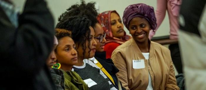 Four women sitting in a row of chairs looking at a presenter and listening intently.