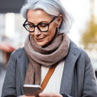 A woman with white hair and glasses looks down at her smart phone