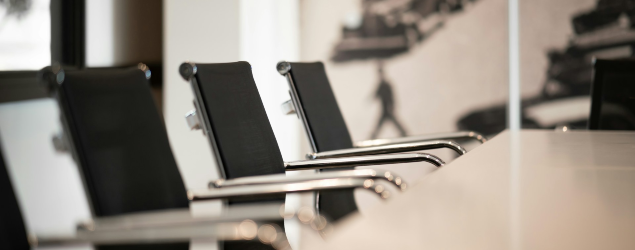 A row of black office chairs is positioned alongside a white conference table in a modern meeting room.