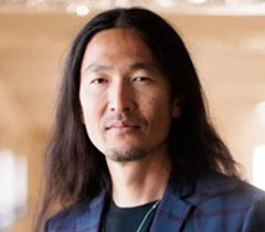 Pak has long, straight black hair and light facial hair.