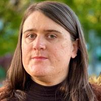 Bacchus has medium length brown hair in a black turtleneck and a winter jacket.