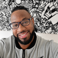 Caleb has dark skin, wears glasses, has a beard, a silver nose ring, and brightly smiles at the camera in a grey bomber jacket. 