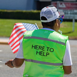 Person with a flag and wearing a vest that says "Here to Help"