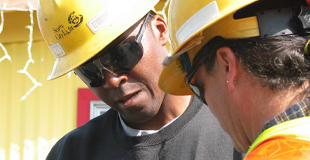Two men in hard hats discuss construction