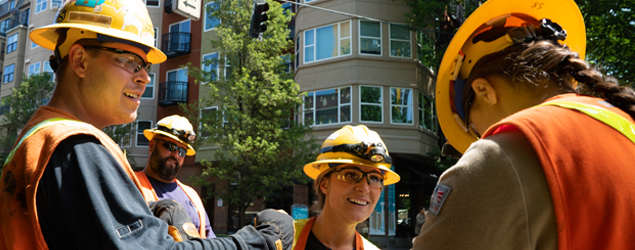 Four workers in safety vests and hard hats working in an urban area