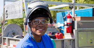 Female welder smiles at the camera in front of her equipment truck