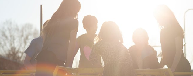 close up of a group of children playing on a mary-go-round with the bright sun causing a flare on the camera lense 