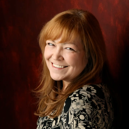 Red headed woman smiling at the camera in front of a red background
