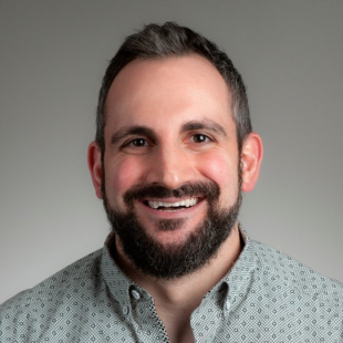 Tom Florino smiling at a camera in front of a grey background
