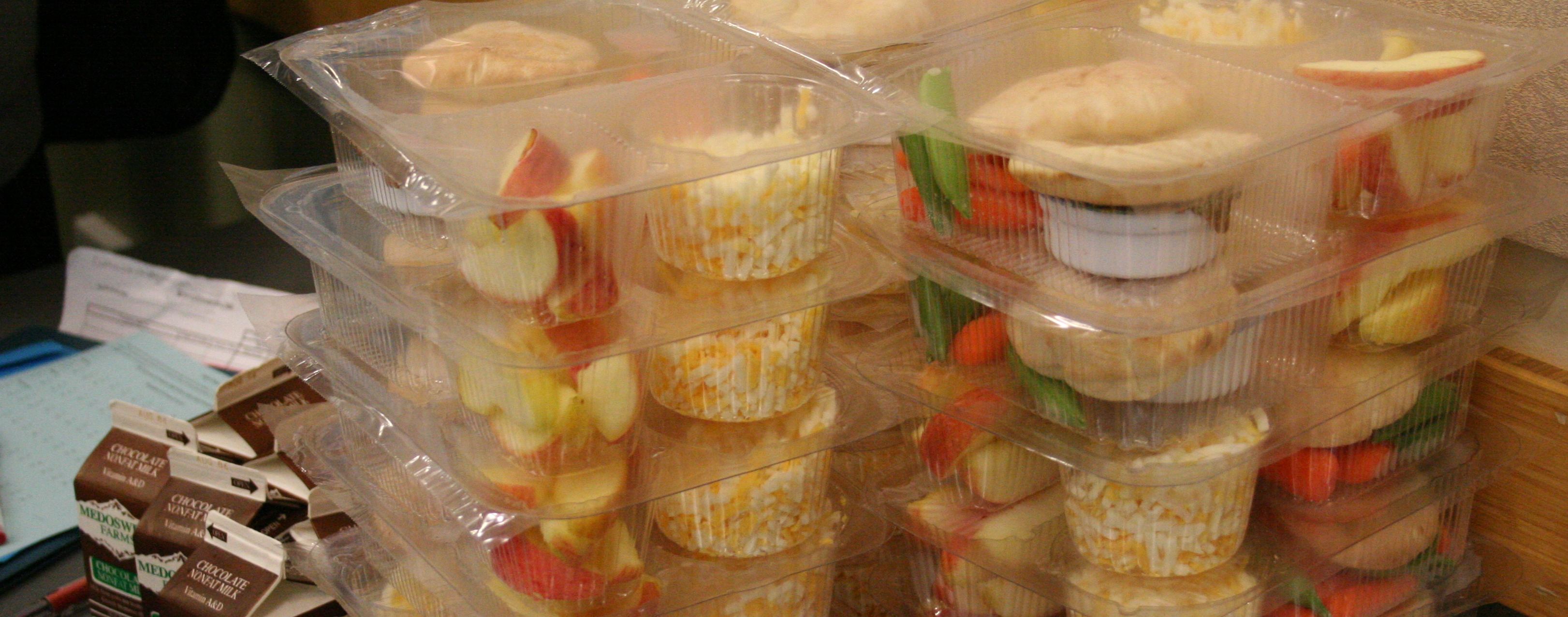 Cartons of milk and snack packages stacked on a table, including rice cakes and apple slices