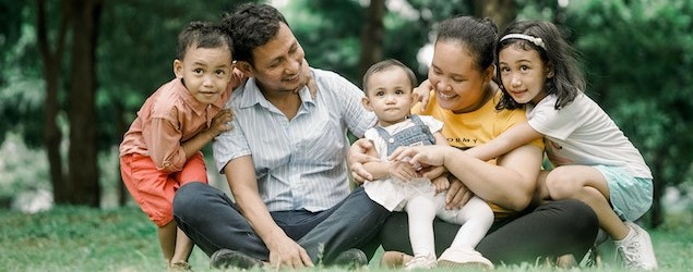 Family photo smiling and sitting on the grass featuring a young boy, father, mother holding a baby, and a young girl [Photo by Migs Reyes on Pexels]