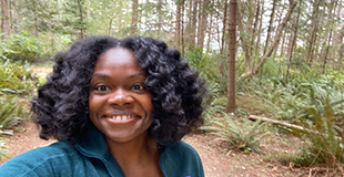 Mary Hall Williams standing in the woods and smilng.