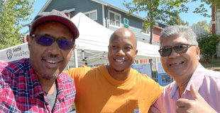 Community engagement coordinator, Alvin, standing and smiling with two community liaisons in the sun.