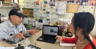 A mechanic looking at a computer with a tech helper in the office of an auto shop.