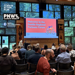 An audience seated in a wood-paneled room facing a large screen reading ‘Welcome to the Seattle Regional Partners Forum