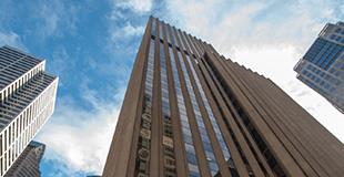 Narrow looking up at a skyscraper with blue sky and other building in the background