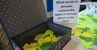 A table with a collection box filled with leaf shaped cards and  asign that says "what words or phrase capture the spirit of climate action in our city"