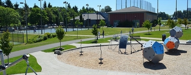 Playground with climbing structures and spinners with a tennis court in the background