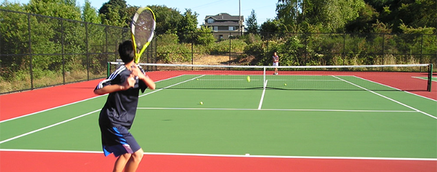 Two people plaing tennis on a bright green court with red clay border