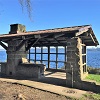 a picnic shelter made of stone, next to a body of water