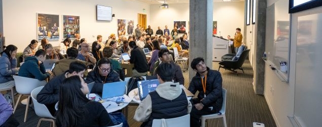 Crowd of hackathon participants listening to a speaker at a podium