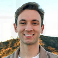 Justin is smiling against a background with a hill and flowers