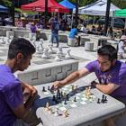 People playing chess in the sunshine, with a giant floor chess set behind them