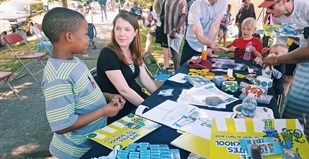 Adults and children look at stickers, bracelets and other walking and biking incentives laid out on a table.